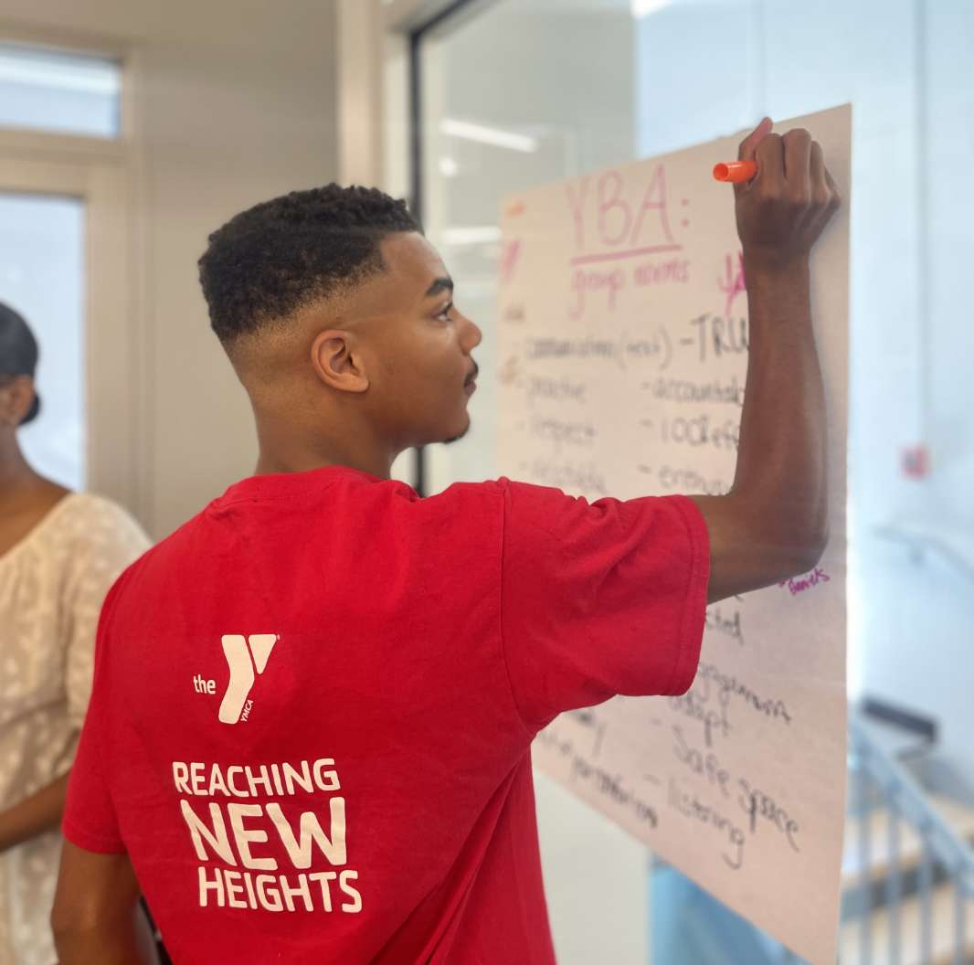 A young African American man wearing a YMCA shirt writing on a poster.